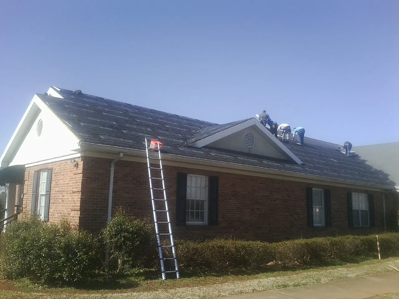 Crew tearing shingles off a brick ranch roof with a ladder set — Emergency Roof Repair work by our crew in Ewing