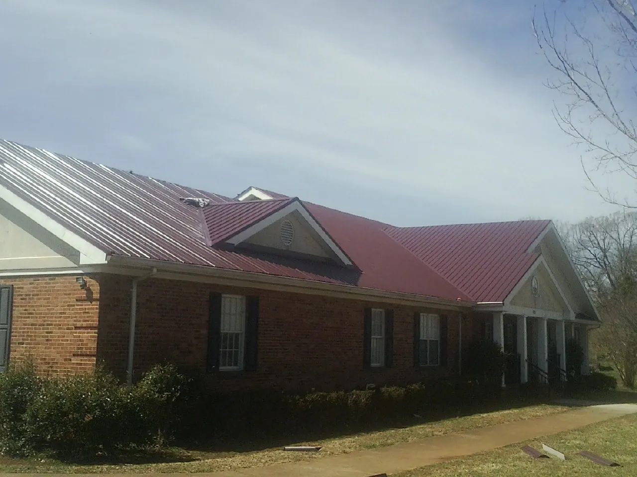 Red metal roof with gabled entries on a long brick building, from a Hail Damage Roof Repair job in Ewing