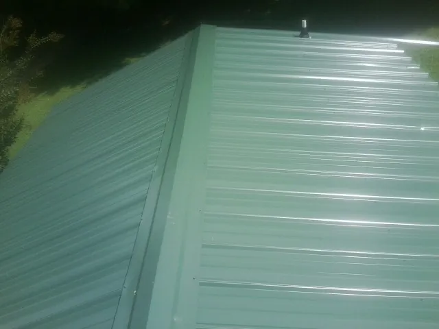 New green metal panels meeting at the ridge of a roof — Flat Roof Repair work by our crew in Ewing