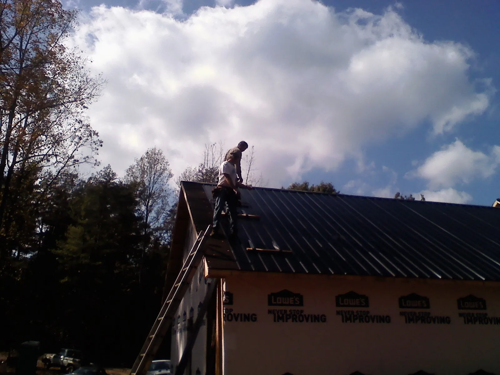 Roofer fastening dark metal panels high against a cloudy sky, from a Roof Inspection job in Ewing
